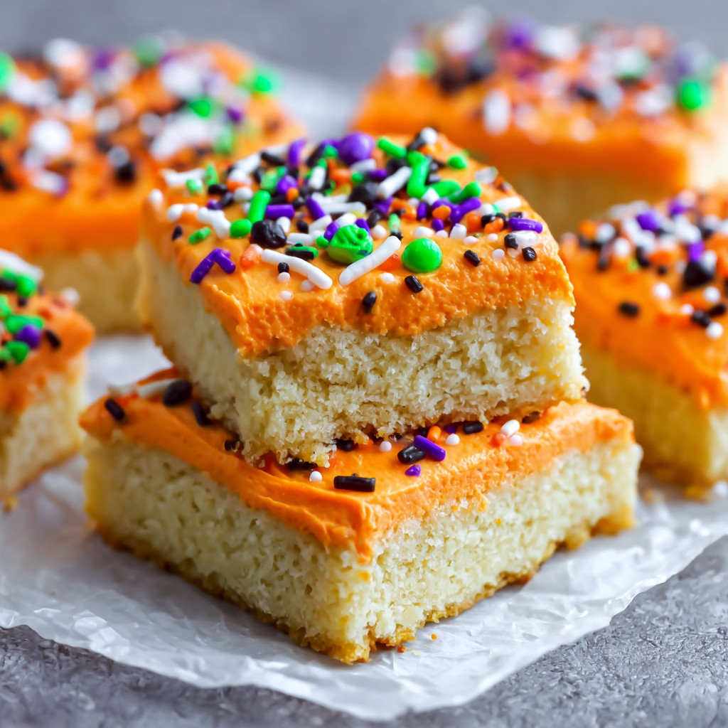 A piece of cake with orange frosting and sprinkles.