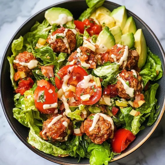 A bowl of salad with meatballs and tomatoes.
