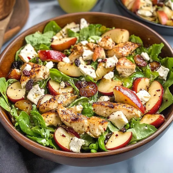 A bowl of salad with chicken, apples, and greens.