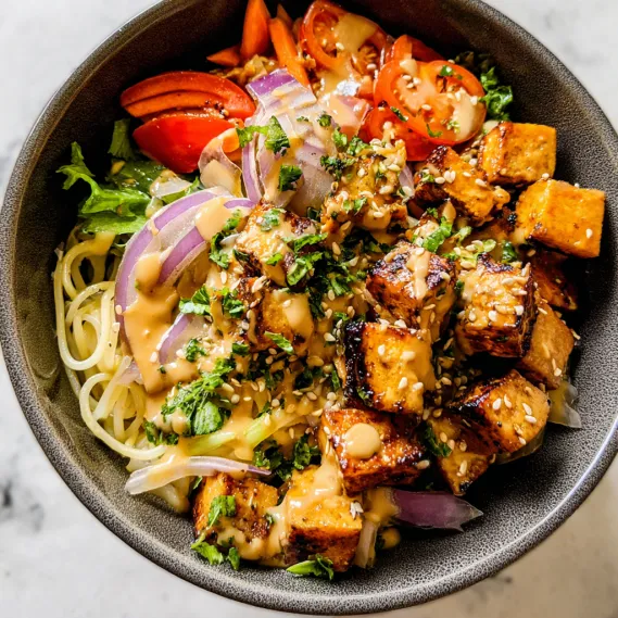 A bowl of food with noodles, tomatoes, onions, and carrots.